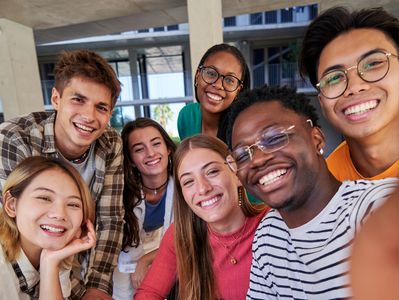 group of young people gathered around a computer, smiling while taking a selfie