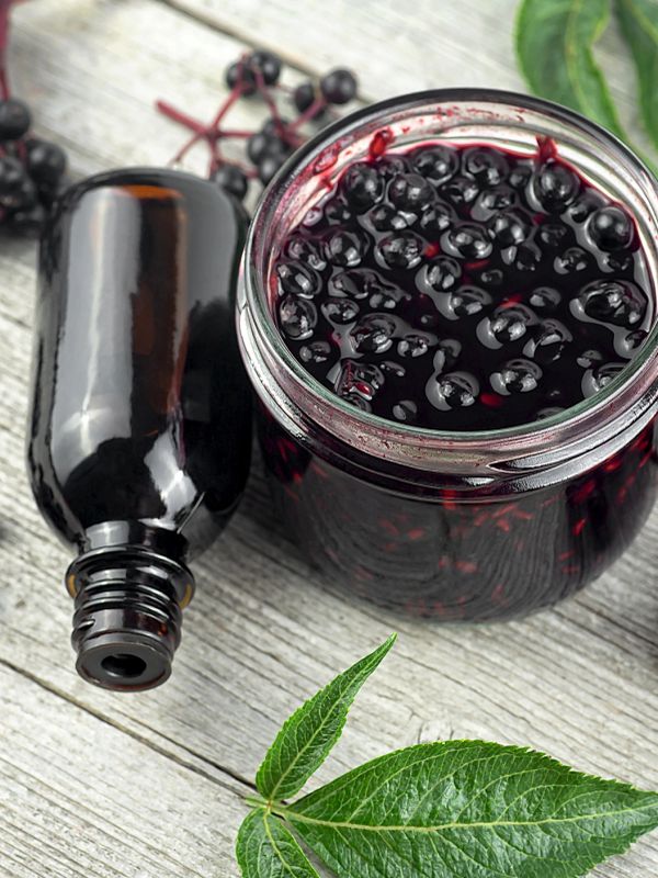 Jar of elderberry syrup and a dark bottle on wooden surface.