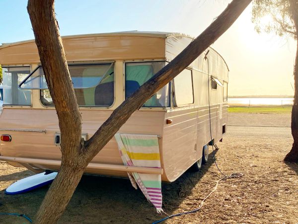 Vintage camper parked near trees by the water at sunset.