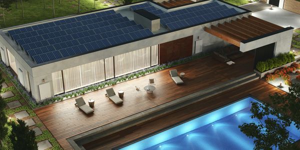 Modern house with solar panels, wooden deck, and illuminated pool at night.