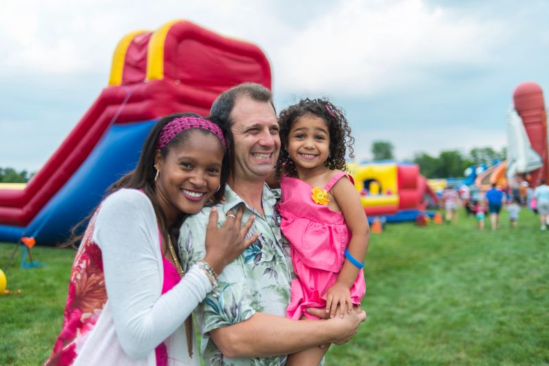 Child and her parents posing for a group photo at a summer festival.