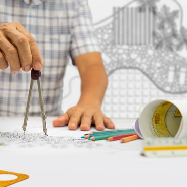 Person using compass on architectural drawing with colored pencils and drafting tools.