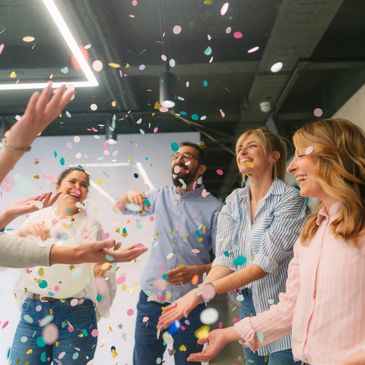 Group of coworkers joyfully celebrating with confetti indoors.