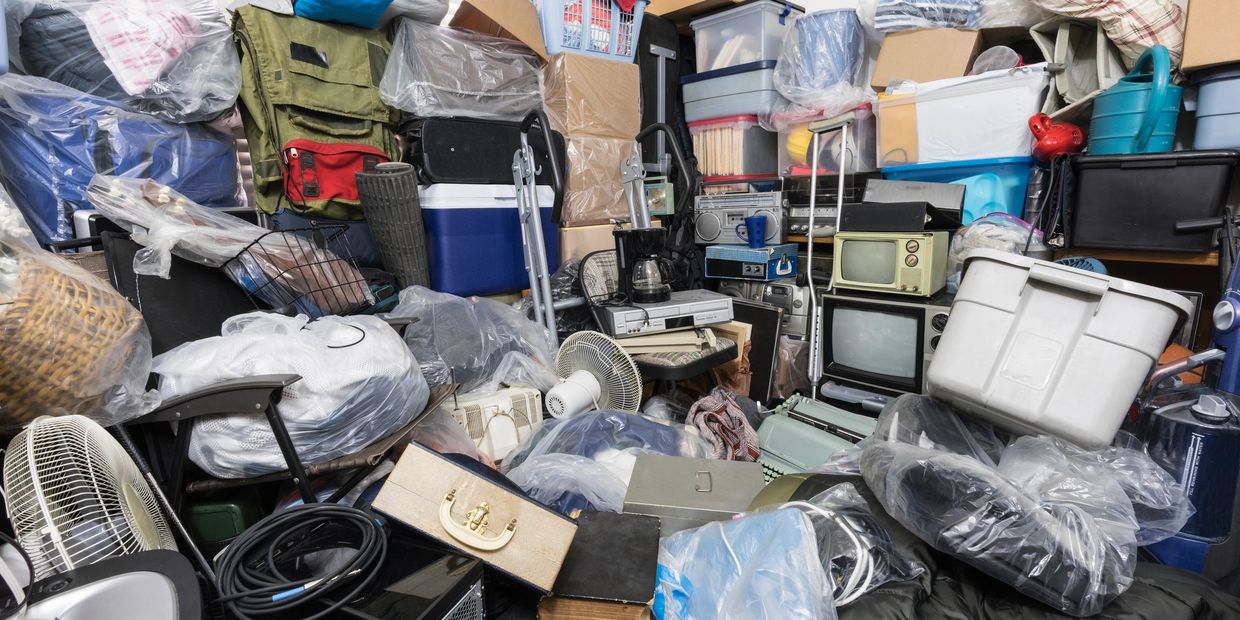 A cluttered room filled with boxes, bags, and household items piled high.
