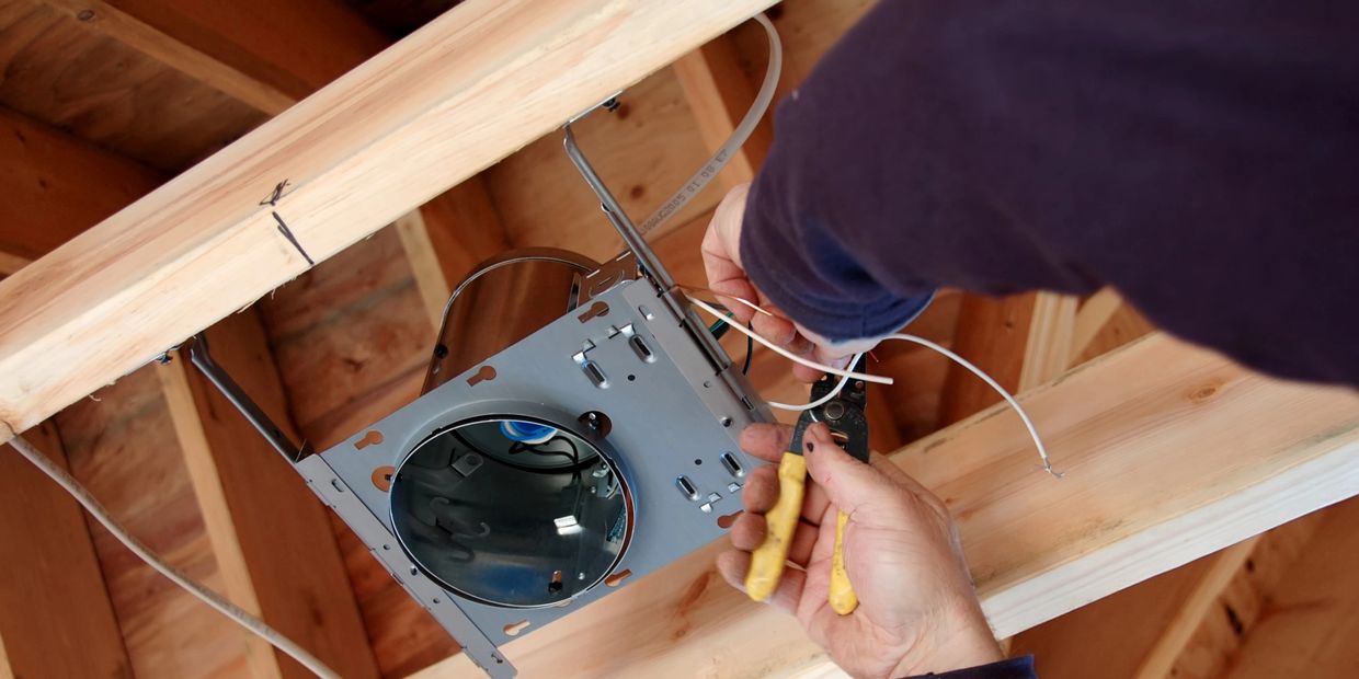 Person wiring a recessed light fixture in a wooden ceiling frame.