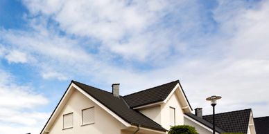 Modern suburban house with a black roof and white walls under a partly cloudy sky.