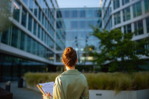 Woman holding an agreement clipboard outside a modern office building.