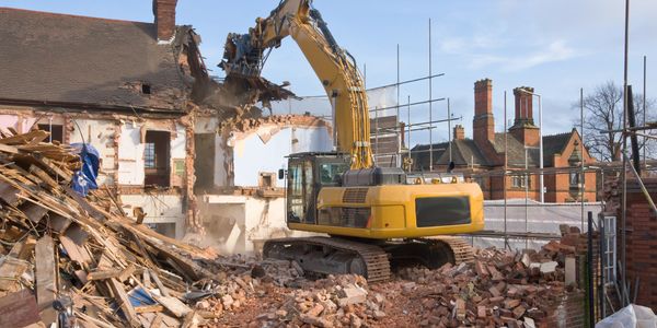 Yellow excavator demolishing an old brick building amid rubble.