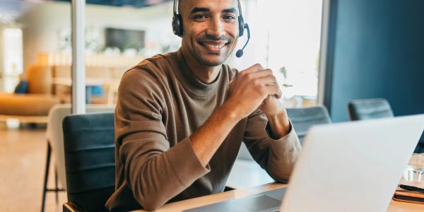 Homem sorridente com headset trabalhando no laptop.