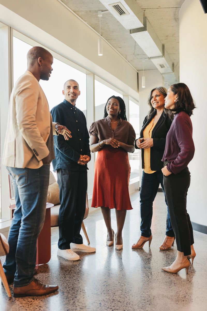 Group of multiracial business partners smiling and listening to businessman talk at meeting in coworking space