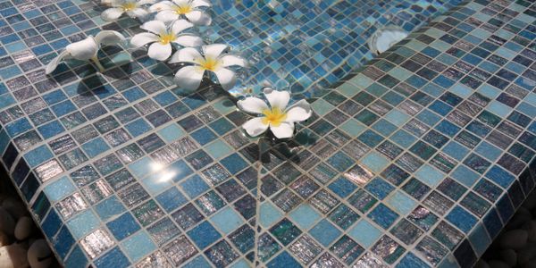 White flowers floating on blue mosaic tiles in water.