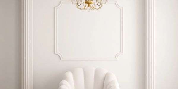 Elegant white armchair with gold accents between two classical columns under a gold chandelier.