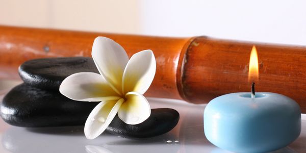 Zen spa setup with black stones, a white flower, bamboo, and a lit blue candle.