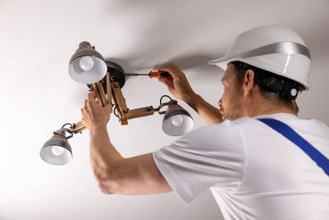 Electrician fixing ceiling light fixture wearing a white helmet.