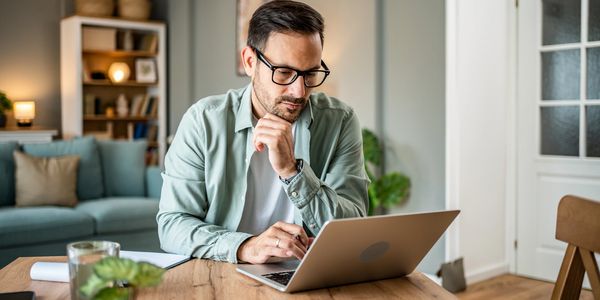 Man working thoughtfully on laptop at home desk.