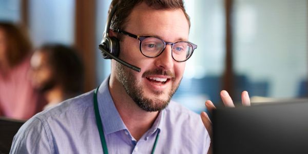 Man with headset smiling at laptop.