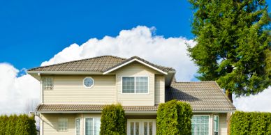 Two-story beige house with a tiled roof under a bright blue sky.