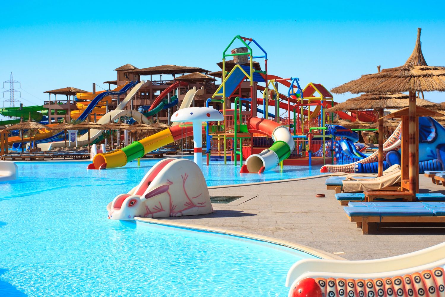 Vibrant water park with colorful slides, clear blue pools, and lounge chairs under a bright sky. 