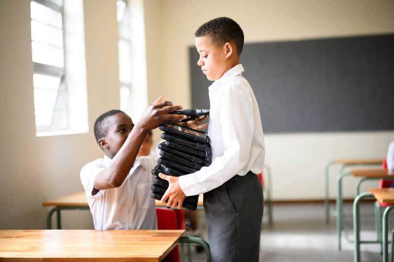 Schoolboy handing out digital tablets for classmates to work on in STEM class