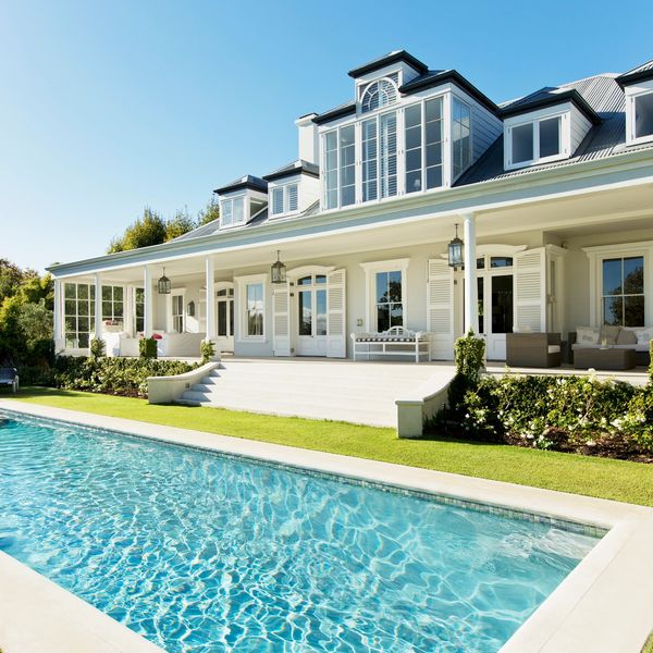 Elegant white house with a large swimming pool and manicured lawn under clear blue sky.