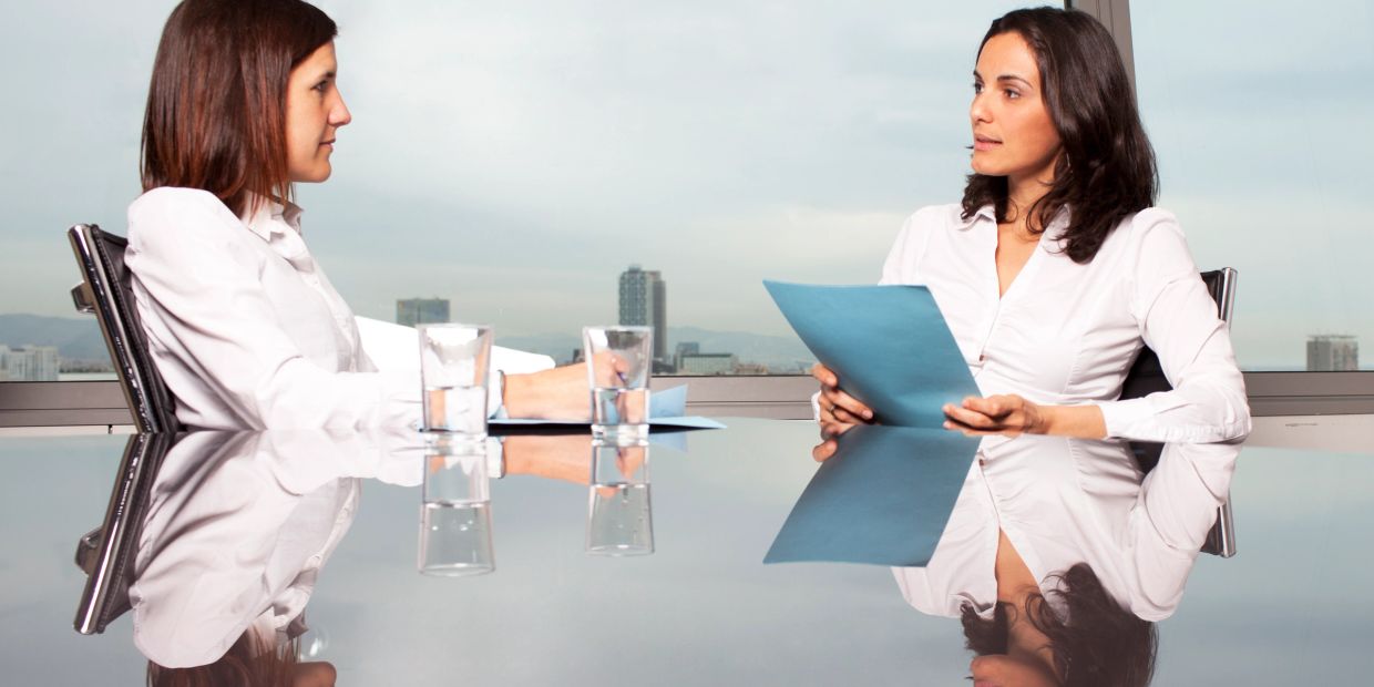 Two women in a business meeting with documents and water glasses.