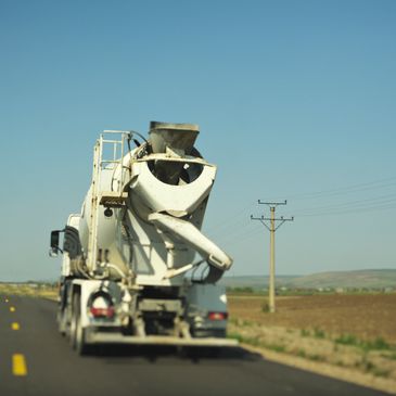 Concrete mixer truck driving on a rural road under clear sky.