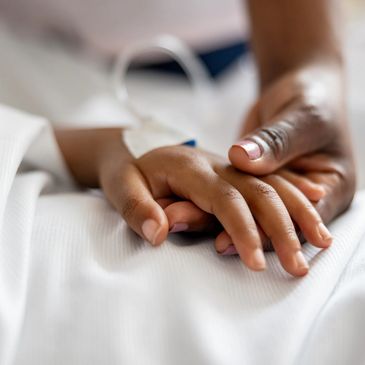 An adult hand gently comforting a child's hand with a hospital wristband.