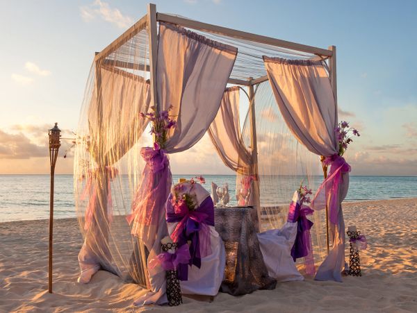 Romantic beach dining setup with purple accents at sunset.