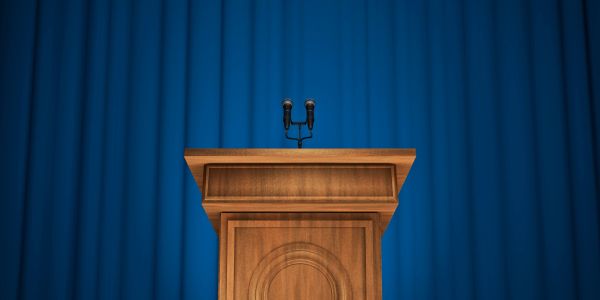 Empty wooden podium with microphones in front of blue curtains.