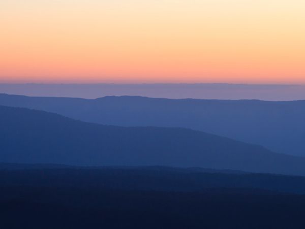 a light orange sky over a misty blue mountain range