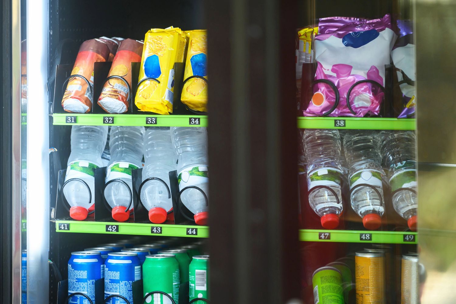 Vending machine stocked with water bottles, snack packs, and soda cans.