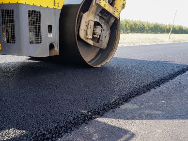 A road roller compacts freshly laid asphalt during road construction.