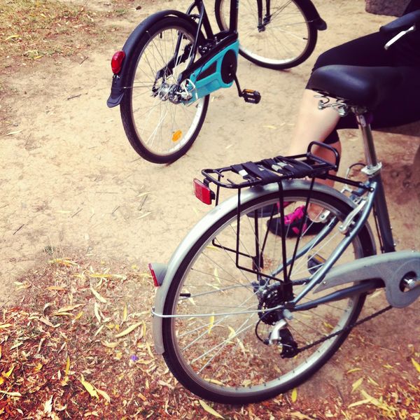 Two bicycles parked on a dirt path with a person sitting nearby.