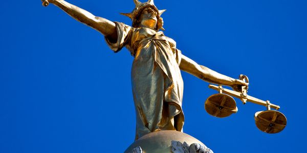 Golden statue of Lady Justice holding a sword and scales against a blue sky.