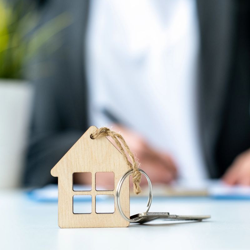 Real estate agent or client signing contract for mortgage on background. Keychain in shape of miniature house and key close up. Concept of home loan and buying own property. Selective focus