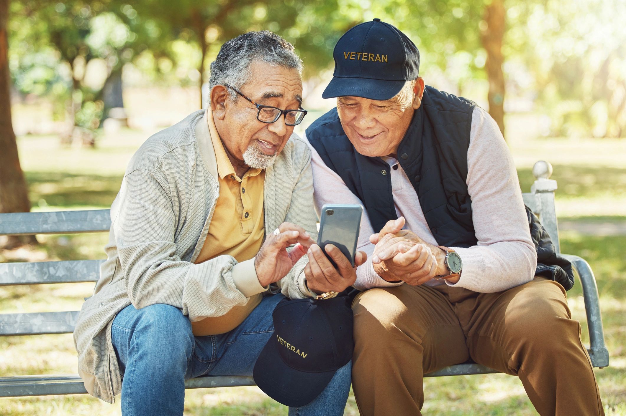 Two elderly men with veteran caps sharing a moment on a park bench.