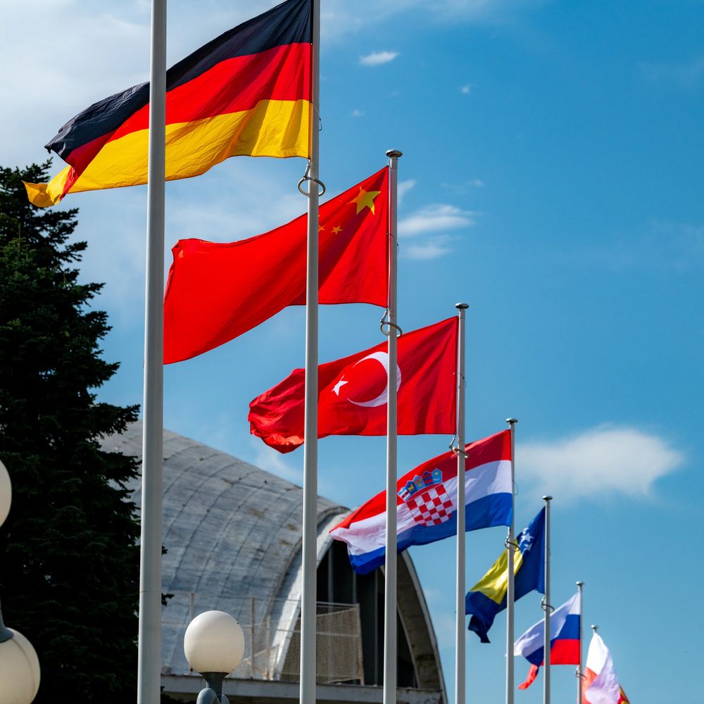 Multiple national flags flying on flagpoles against a blue sky.