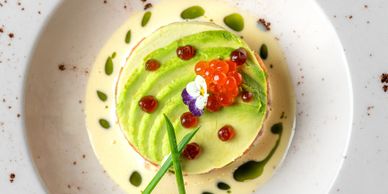 Elegant gourmet dish with avocado, roe, and edible flowers on a creamy sauce.