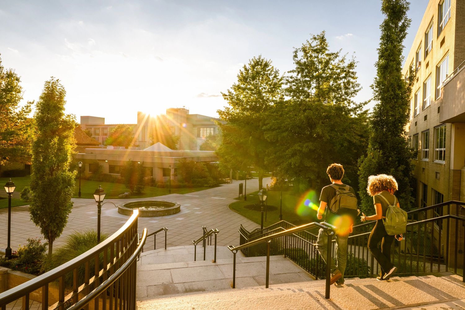 Two students walking down campus steps at sunset with backpacks.