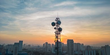 Telecommunication tower at sunset over a city skyline.