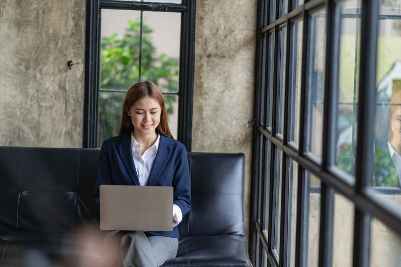 Beautiful young Asian woman using laptop computer, entertaining with social media, relaxing, smiling and laughing. Freelance woman working in online sales marketing