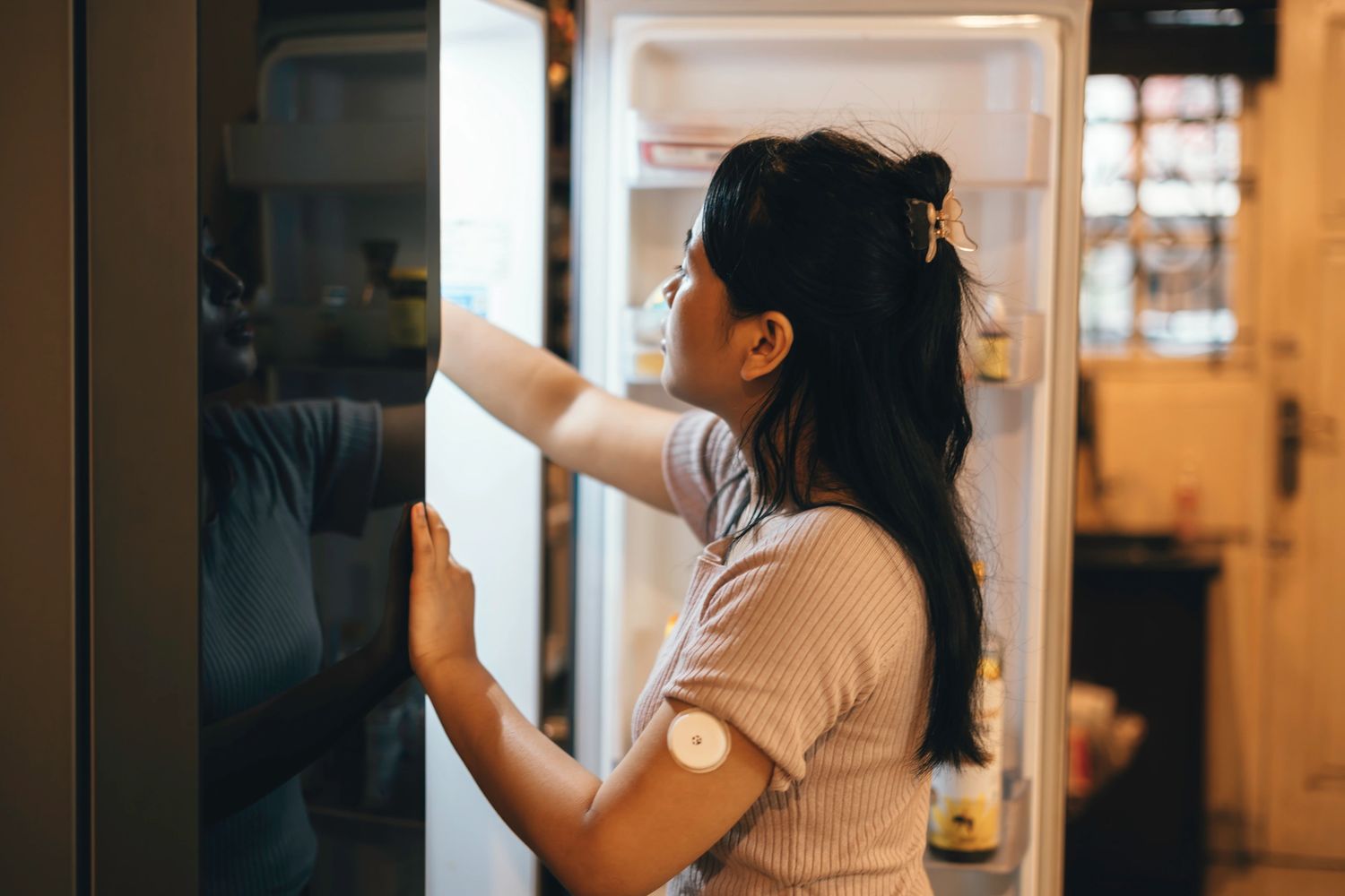 A woman wearing a cgm device opening a refrigerator