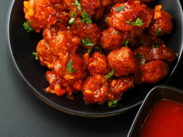 Spicy, saucy Indian-style chili cauliflower garnished with fresh herbs.