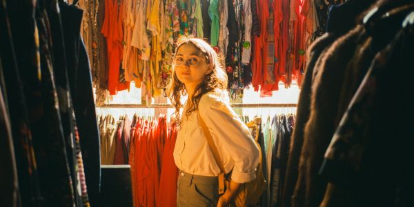Woman browsing colorful clothes in a warmly lit shop.