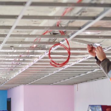 Worker installing ceiling framework with visible wiring and tools.