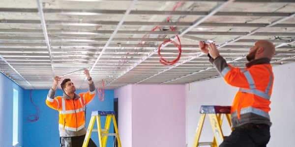 Two workers installing ceiling wiring.