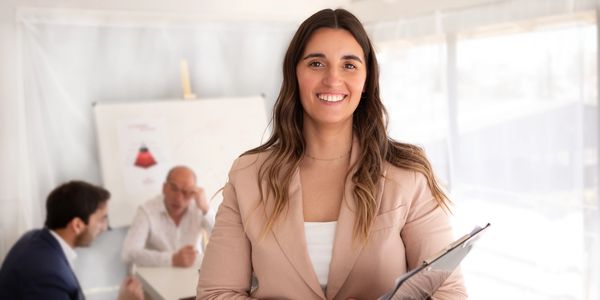 Smiling businesswoman holding a clipboard in a modern office meeting.
