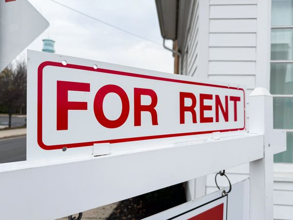 A white and red 'For Rent' sign outside a house.
