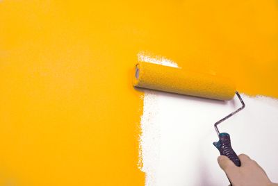 Painting a wall bright yellow with a roller.