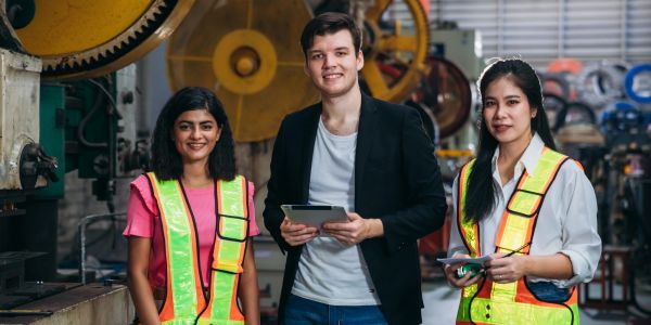 Três trabalhadores em fábrica usando coletes refletivos.